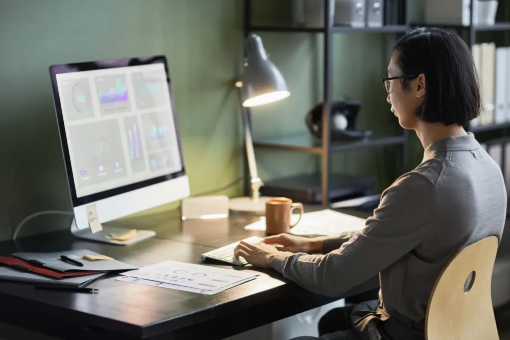 A designer reviewing a data dashboard on a large monitor at a home office desk