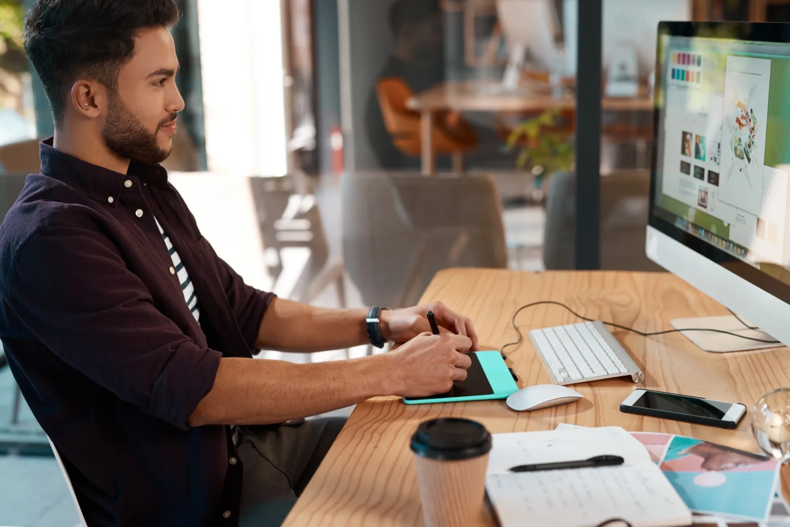 A product designer working on interface screens at a desk with a drawing tablet