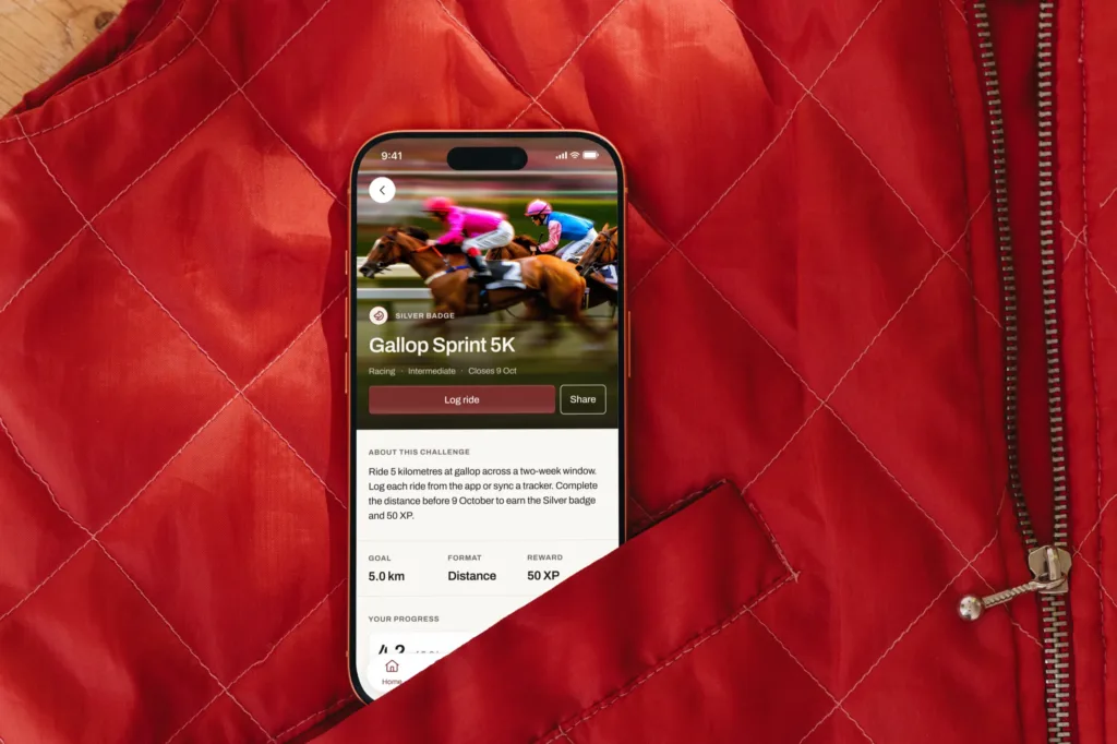 The Bridlepath challenge screen on an iPhone resting on a red quilted riding jacket