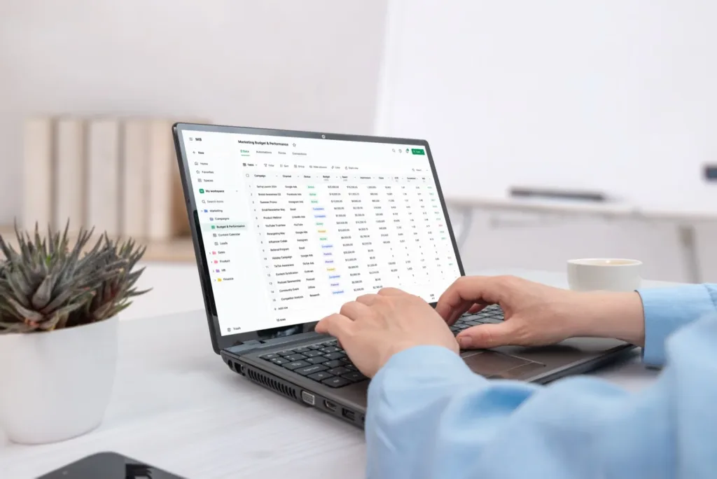 A B2B data table with status chips, filters and sort controls on a laptop, hands on the keyboard