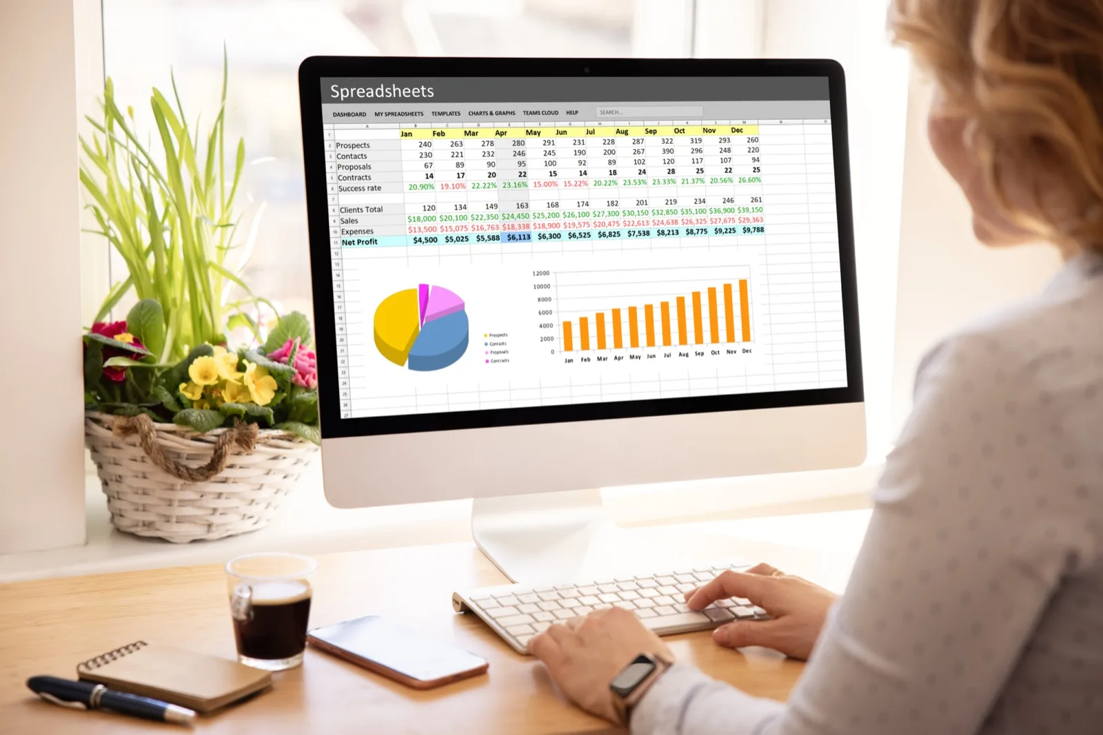 An analyst working through rows of monthly figures in a spreadsheet on a desktop monitor
