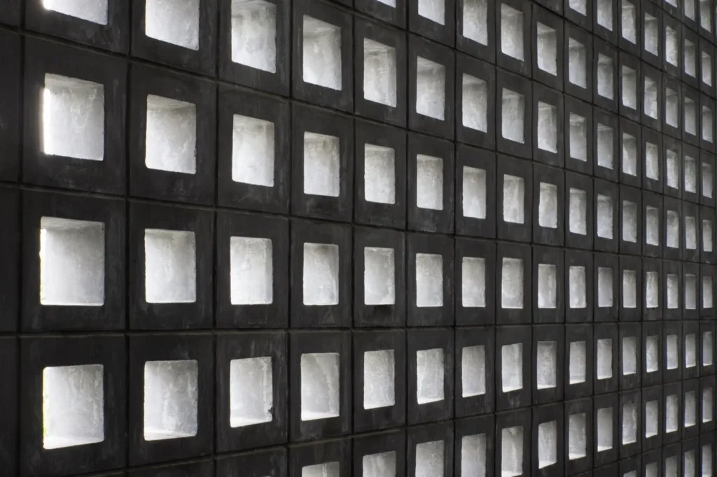 A dark concrete block wall in perspective, light through each identical opening