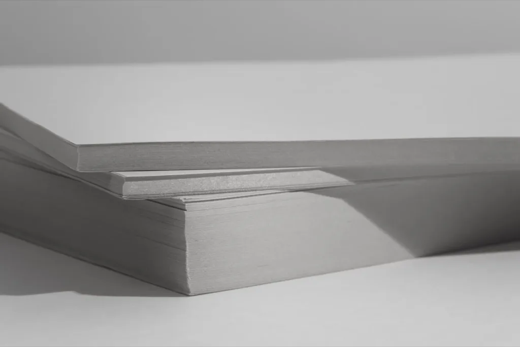 Two stacks of blank white paper under hard light, one resting on the other, in black and white