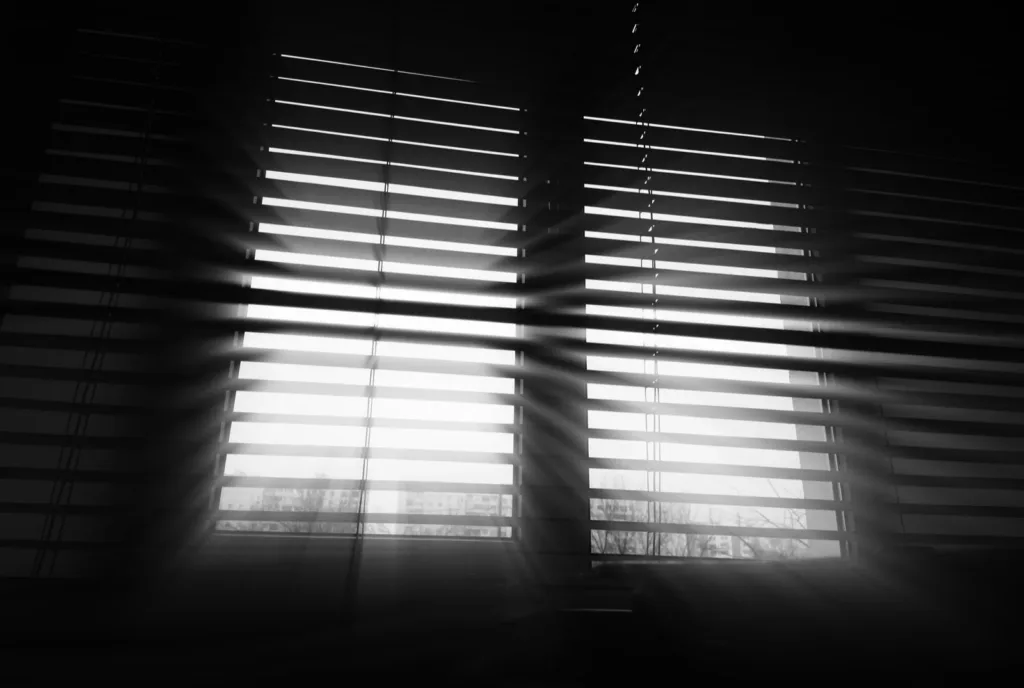 Office window blinds with light breaking through the slats, in black and white