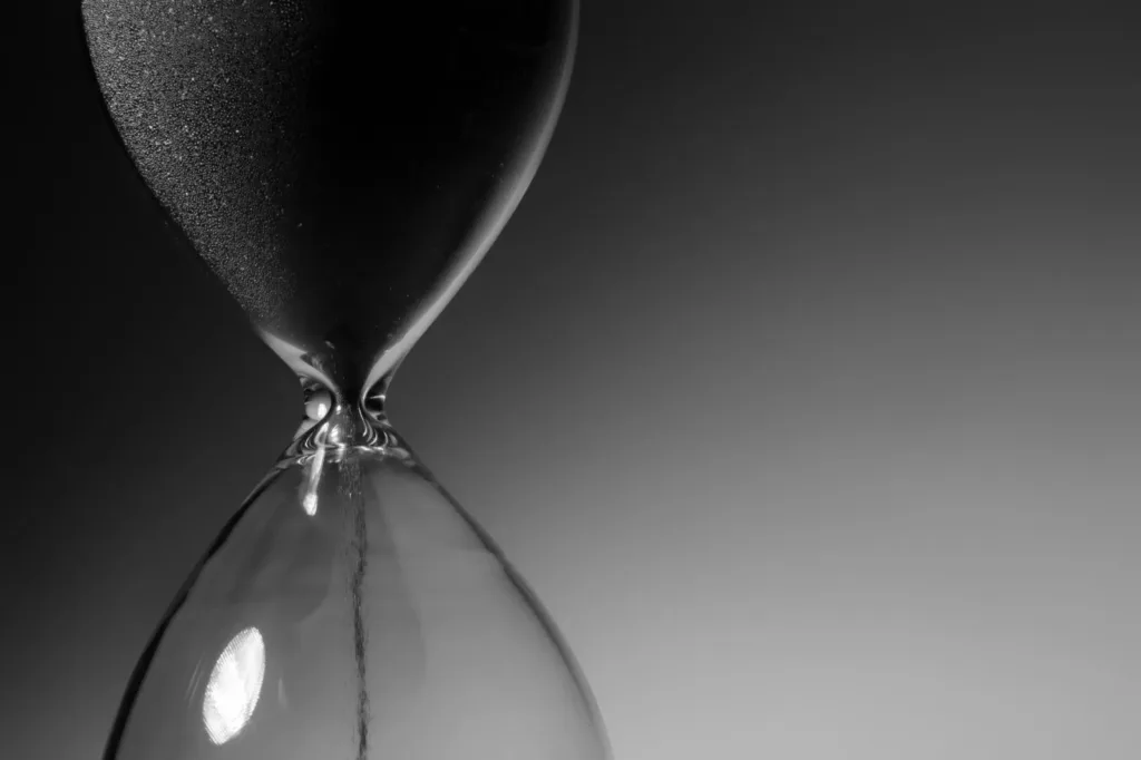 A black and white close-up of an hourglass with sand running through its neck