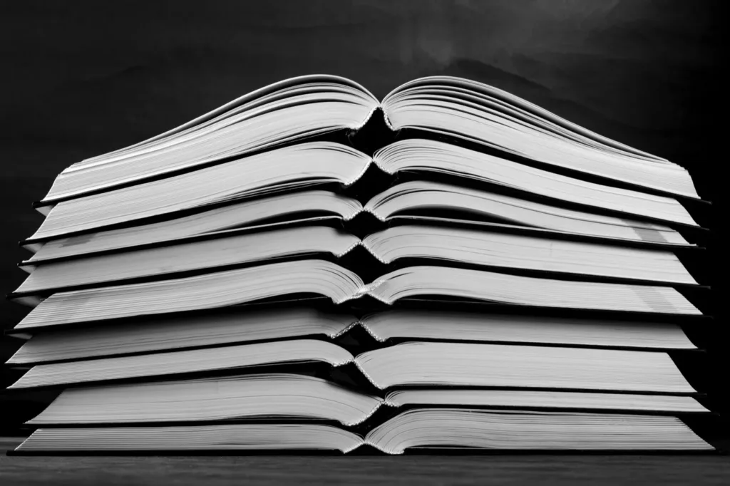 Nine open books stacked on top of each other in black and white