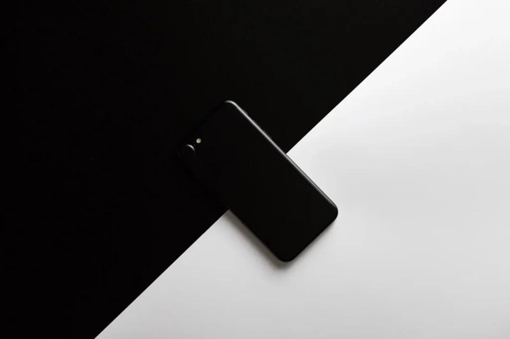 A black smartphone lying on a surface split diagonally into black and white