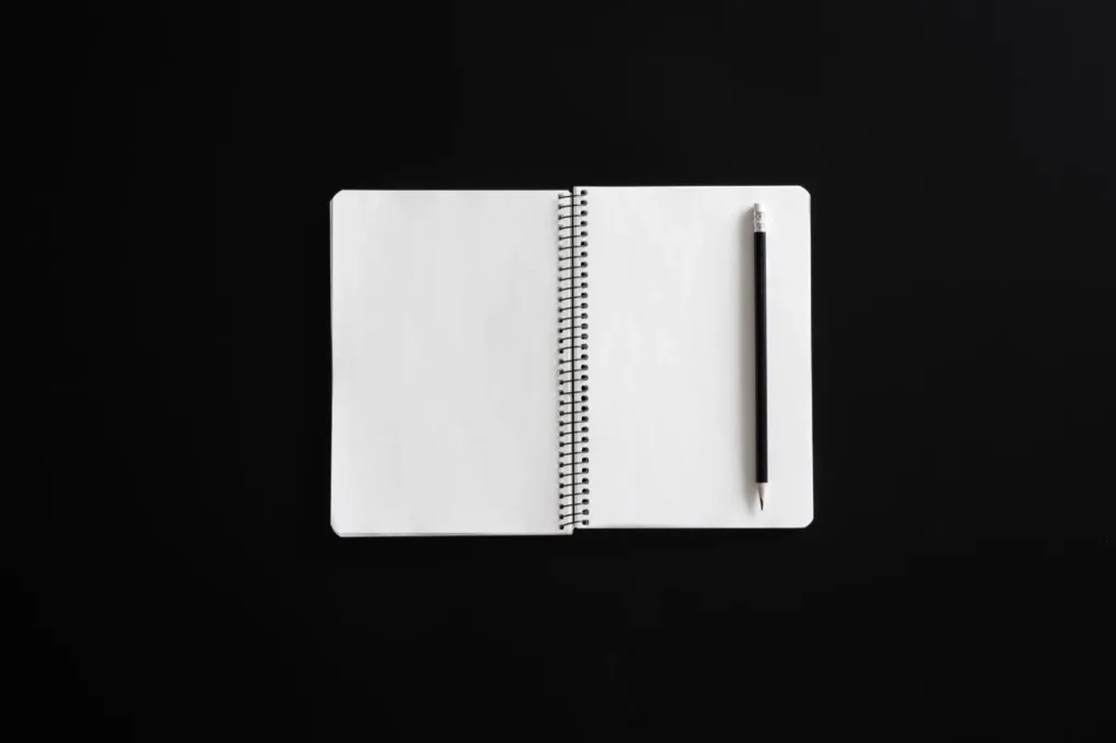 An open blank spiral notebook with a pencil on a black surface