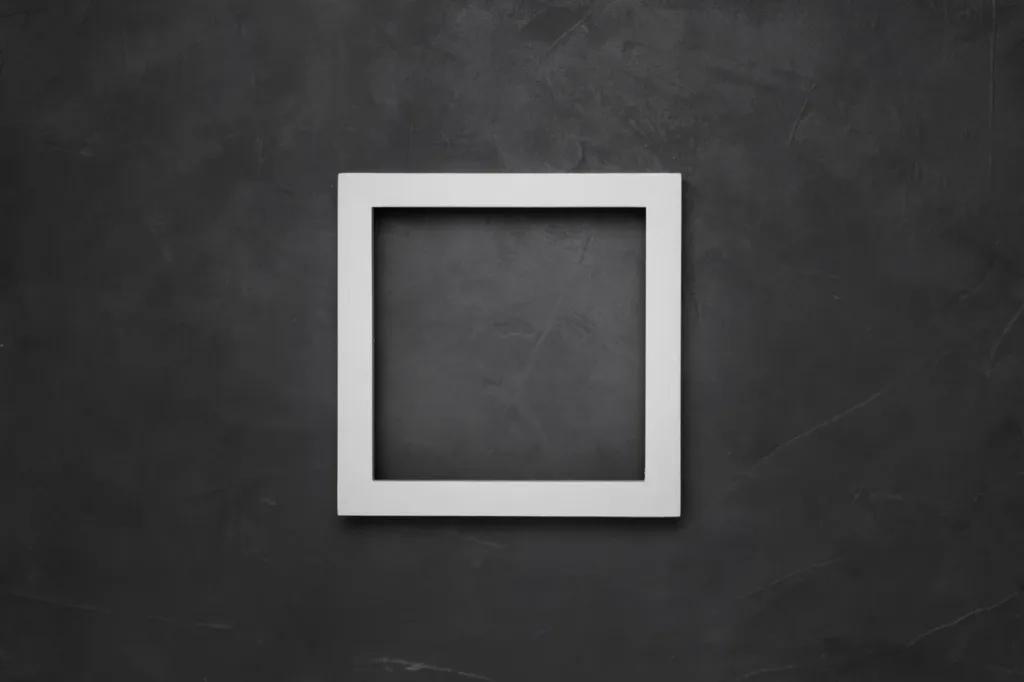 An empty square white frame on a dark plaster wall