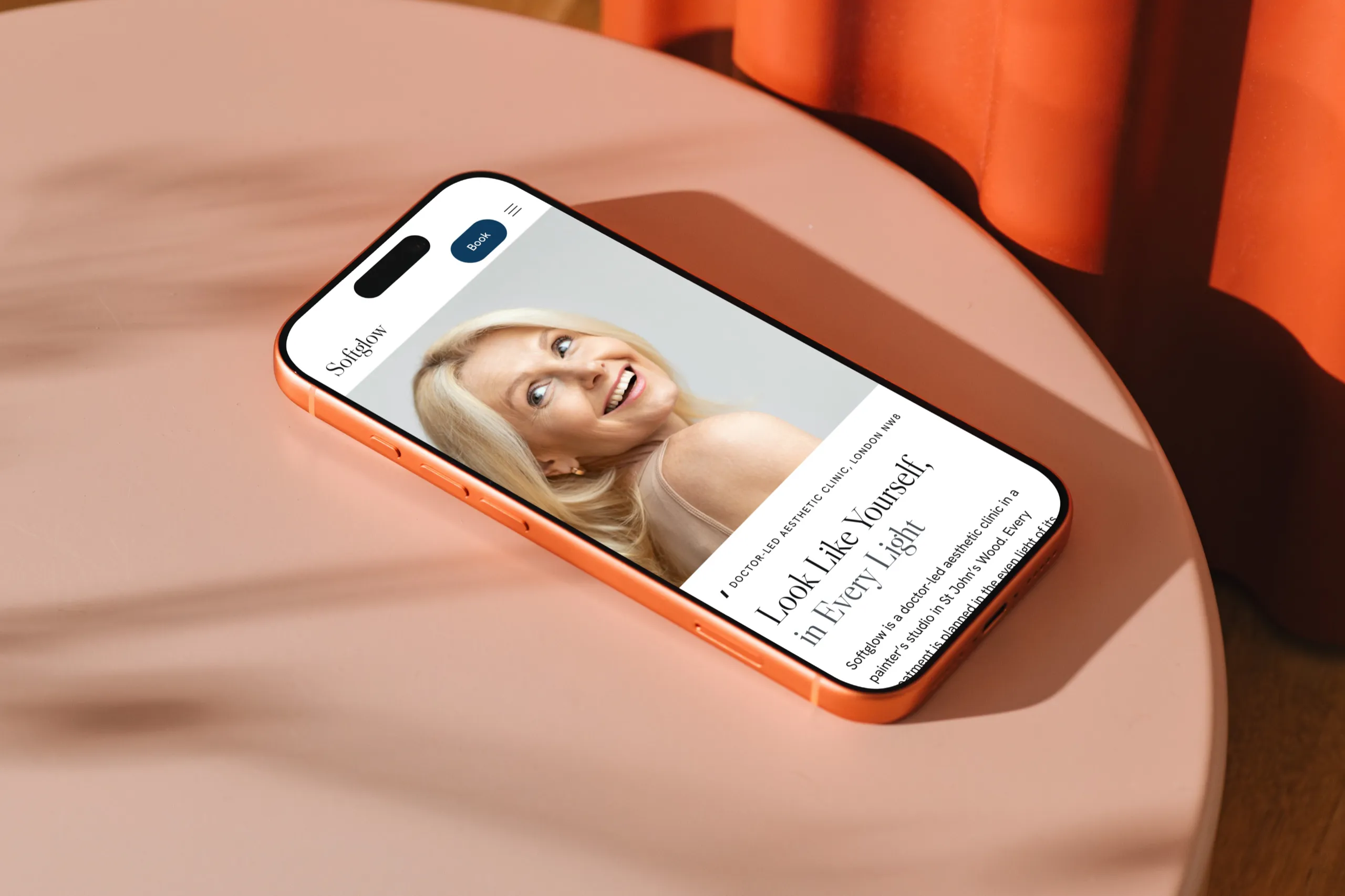 The Softglow homepage on an orange iPhone lying on a pink round table in afternoon sun