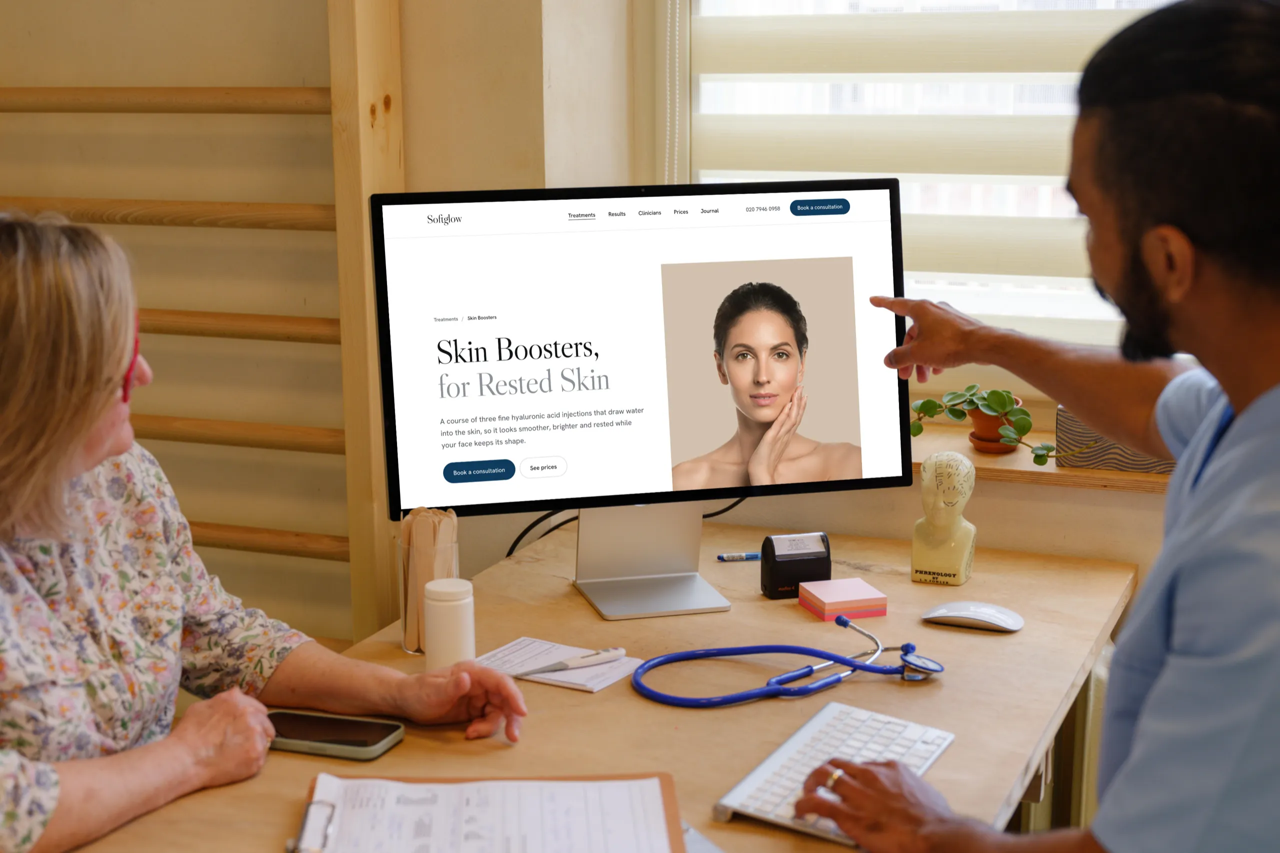 A doctor points at the Softglow skin boosters page, Skin Boosters for Rested Skin, on a Studio Display while a patient looks on