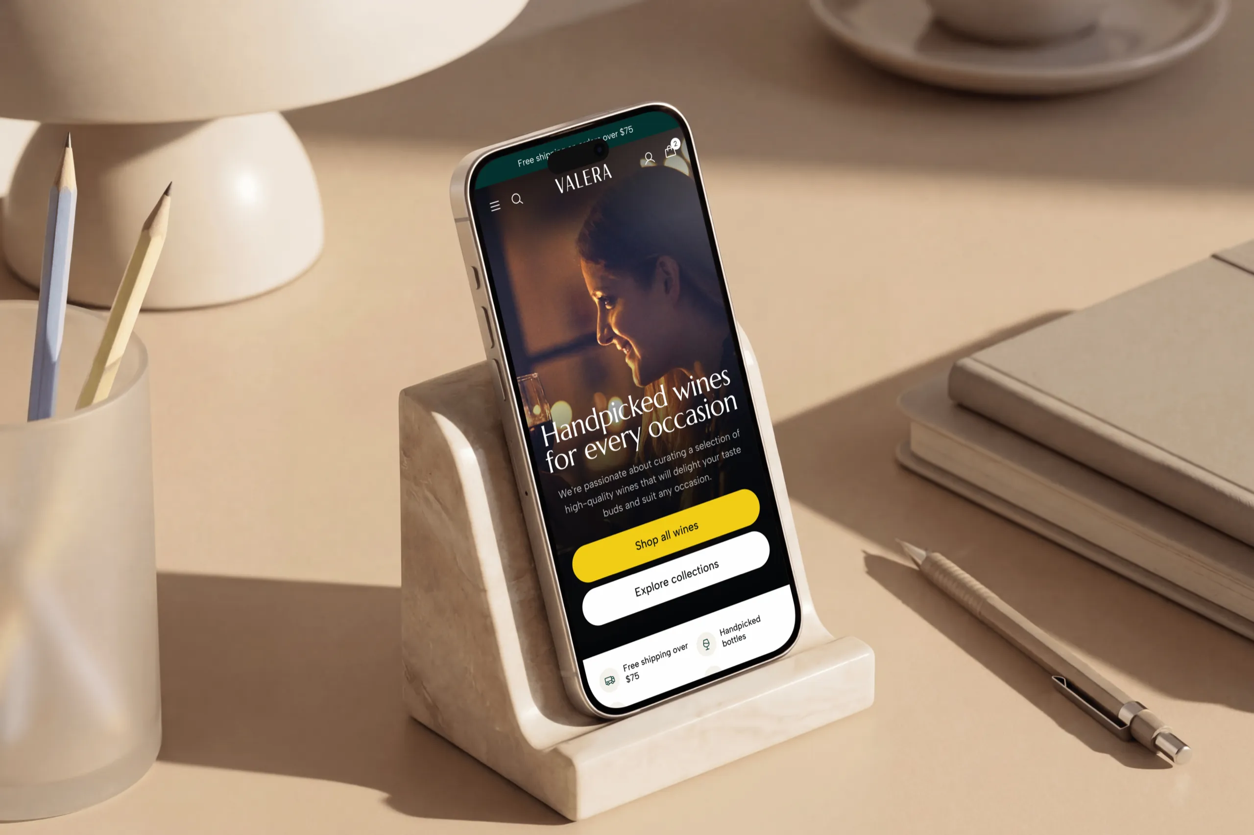 The Valera homepage, Handpicked wines for every occasion, on an iPhone in a marble stand on a beige desk