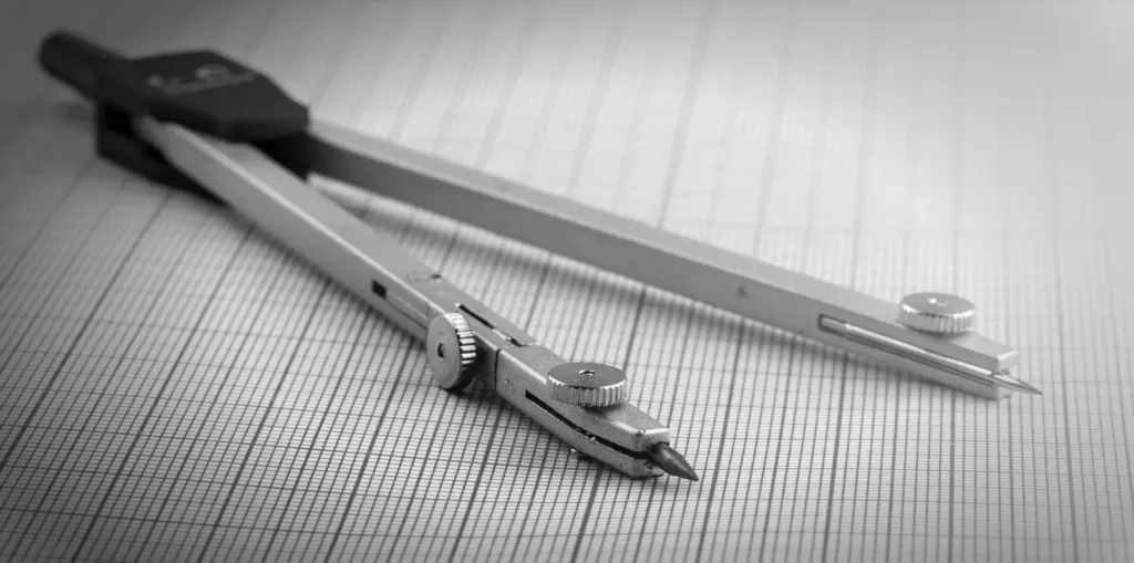 A metal drafting compass lying on graph paper