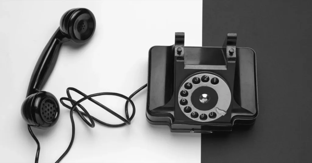 A black rotary telephone with its receiver lifted off, on a background split into white and dark grey